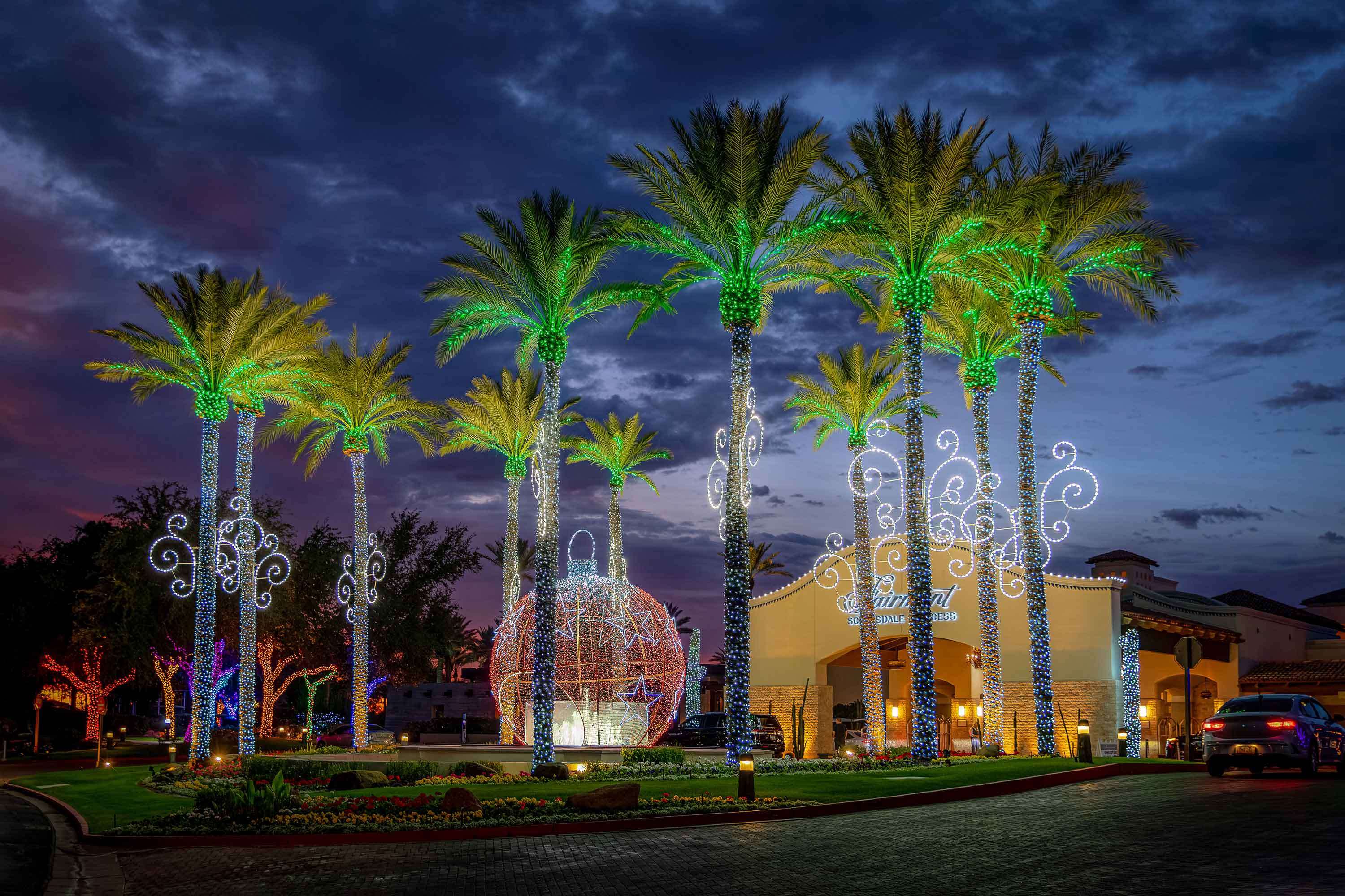 Rows of tall palm trees wrapped in colored LED lights at the entrance to the Fairmont Scottsdale Princess resort.