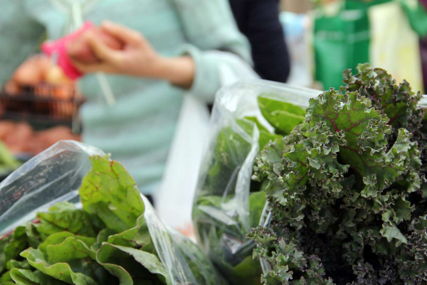 Closeup view of fresh, curly green kale and mustard greens packaged in clear plastic bags at a market stand in Scottsdale.