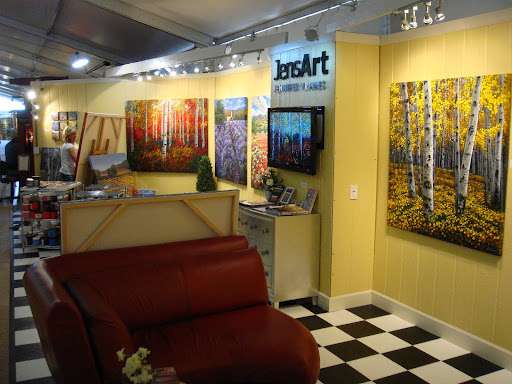 An art booth setup for JensArt Fine Art, featuring landscape paintings on a yellow wall & a red sofa in the foreground.