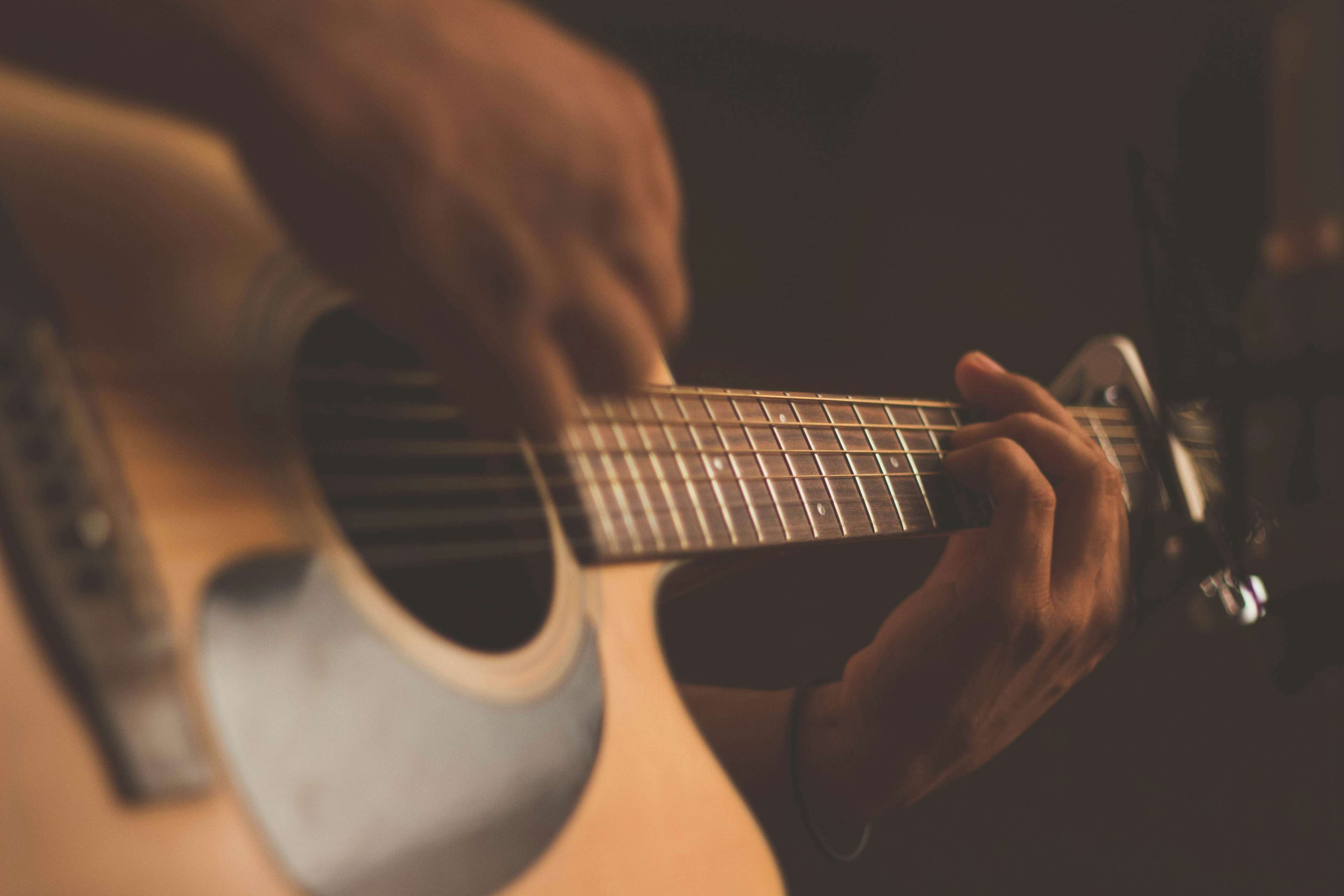 A close-up of a person playing a steel-string acoustic guitar, focusing on the fretboard and soundhole of the instrument.