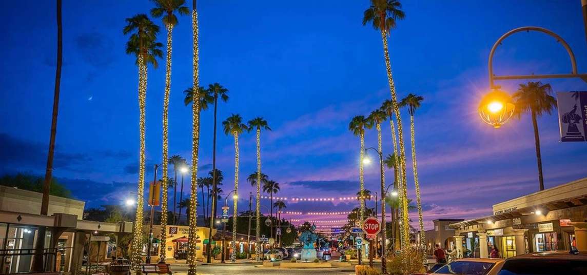 The Scottsdale Arts District in Old Town Scottsdale, tall palm trees wrapped in warm string lights among various shops.